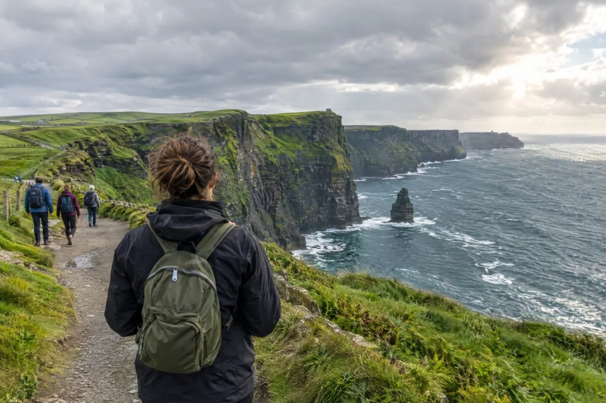 Solo traveler with a daypack on a clifftop path on the west coast of Ireland, with fellow group members walking ahead