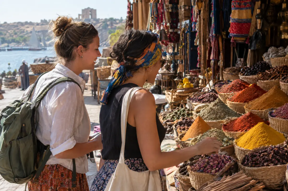 Two women travelers chatting while browsing a colorful spice stall in a market in Aswan, Egypt